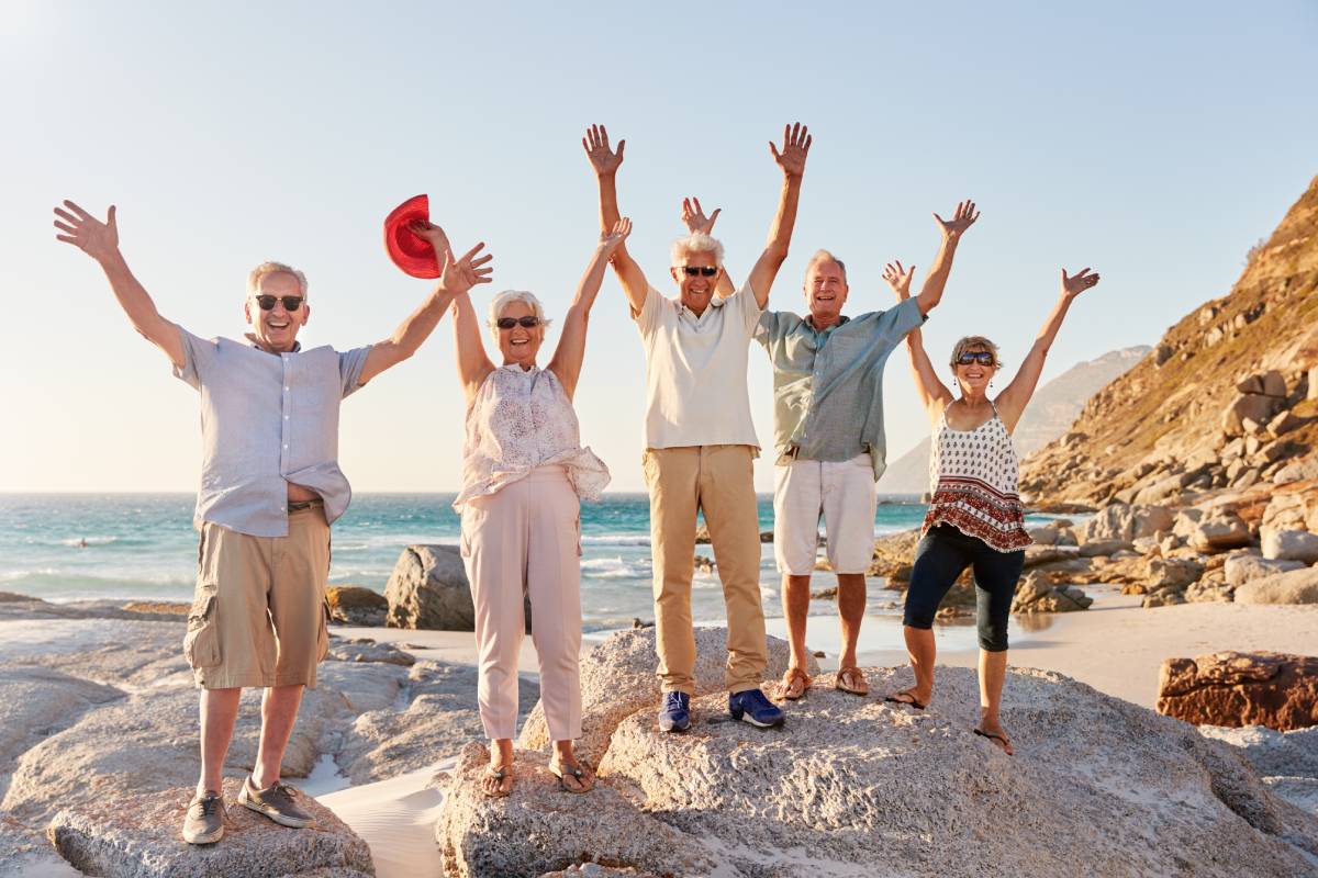 Group of older travellers posing on a beach budget senior travel